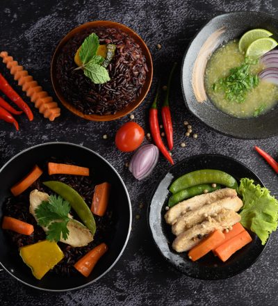 Assorted food and dishes of vegetables, meat and fish on a black stone background. Top view.